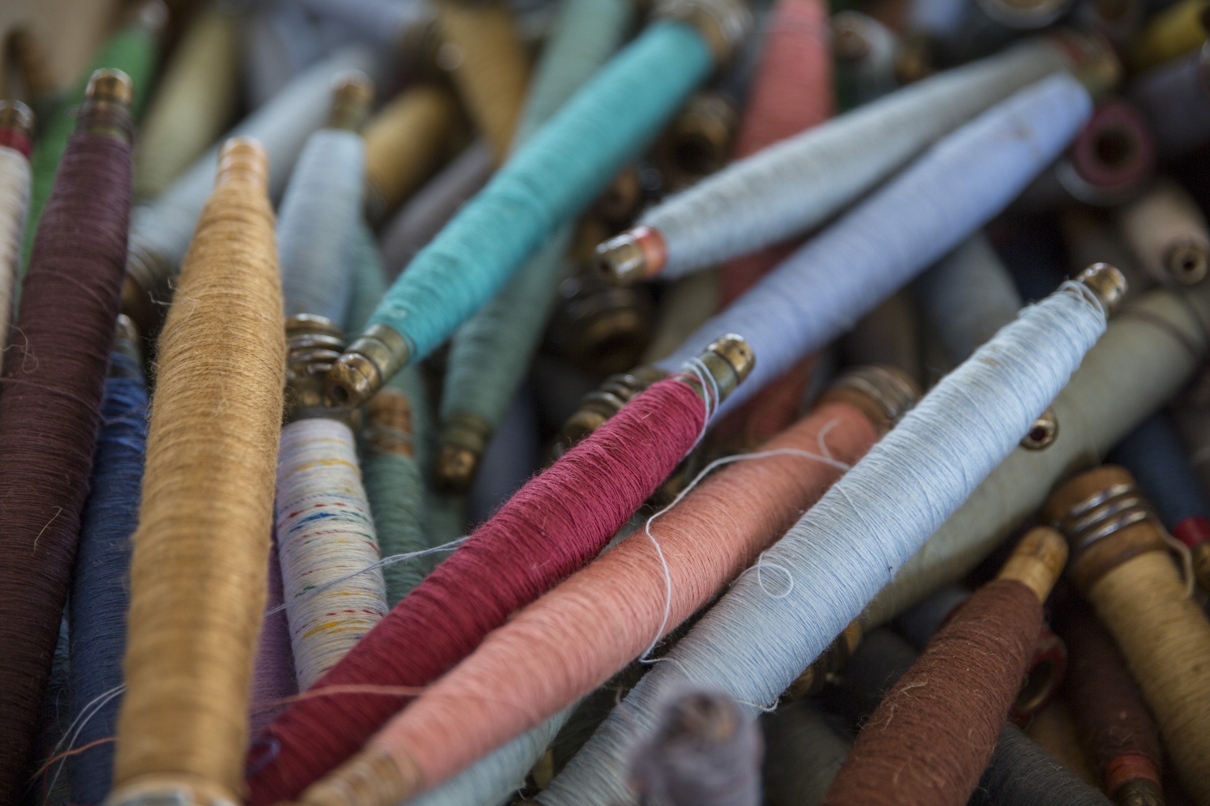A heap of wooden bobbins wound with coloured yarn
